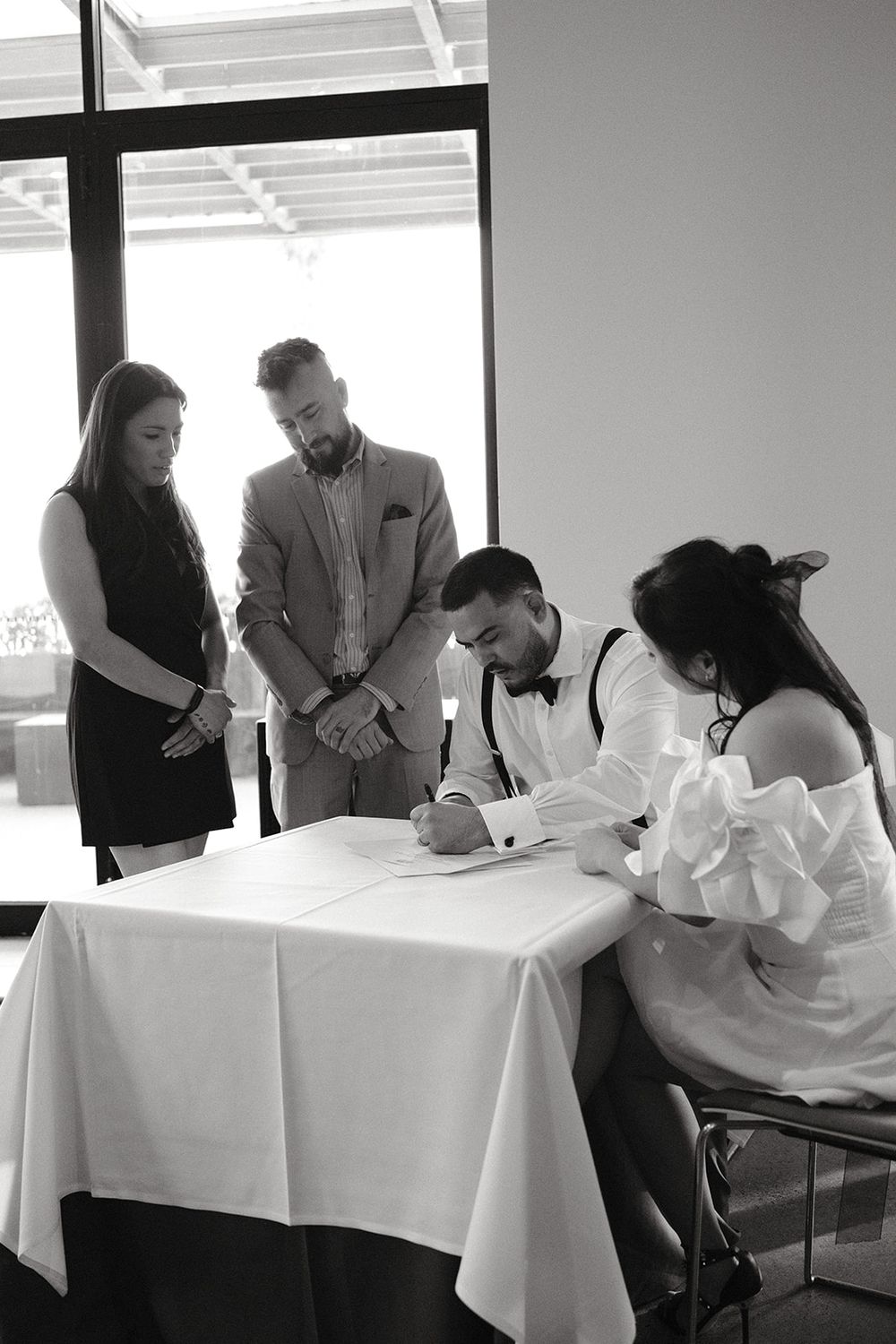Black and white photograph of Deb signing the marriage certificate with Mickey and Josh beside her