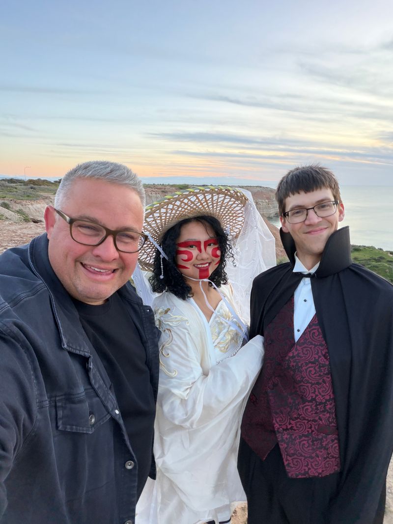 Josh Withers, Jamie and Evan smiling for a selfie above Maslin Beach at sunset, with coastal cliffs and the sea behind them