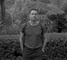 Black and white portrait of wedding photographer Jason Lucas standing among ferns with a backpack