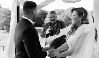 Josh Withers holding a microphone while conducting an outdoor wedding ceremony