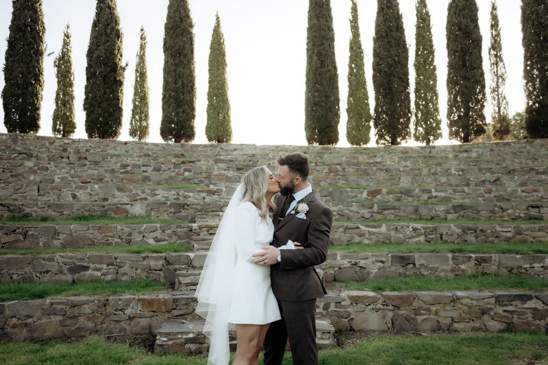 Kaitlyn and Russell kissing beneath the cypress trees in Piermont Retreat’s stone amphitheatre