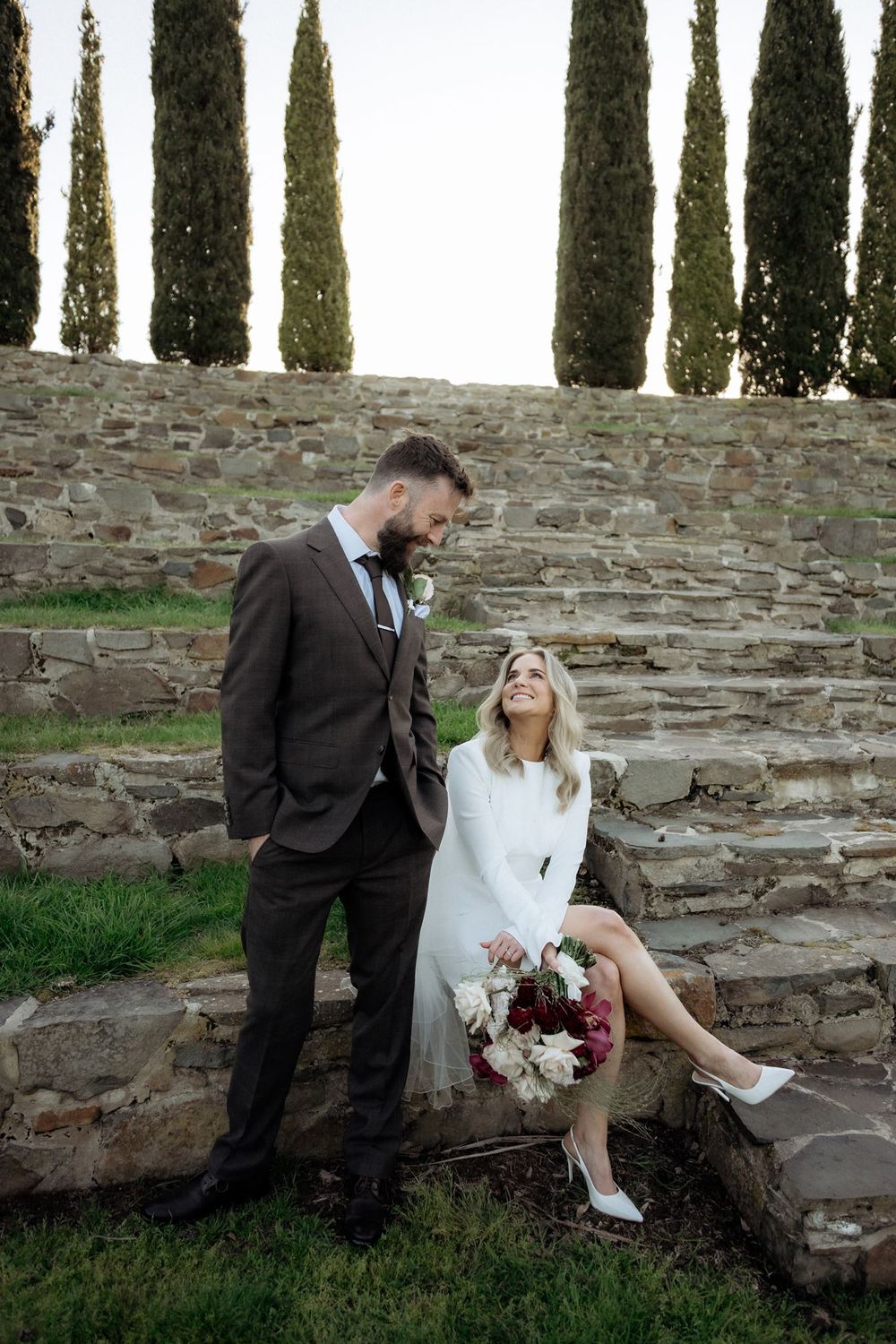 Kaitlyn laughing with Russell while seated on Piermont’s stone steps with her bouquet