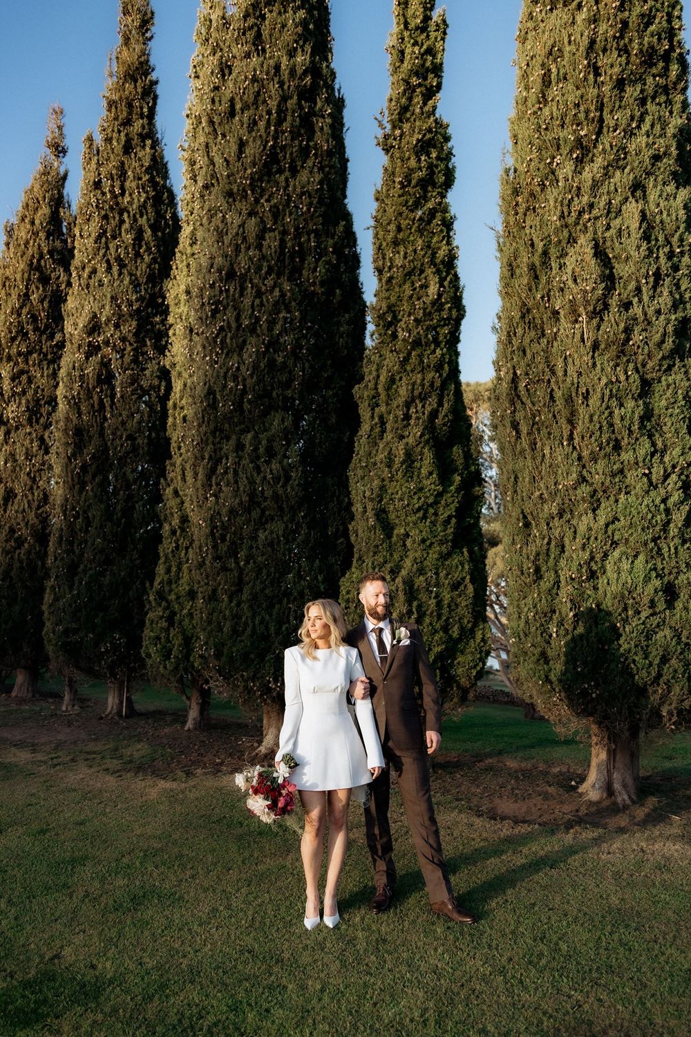 Kaitlyn and Russell standing together beneath the tall cypress trees at Piermont Retreat