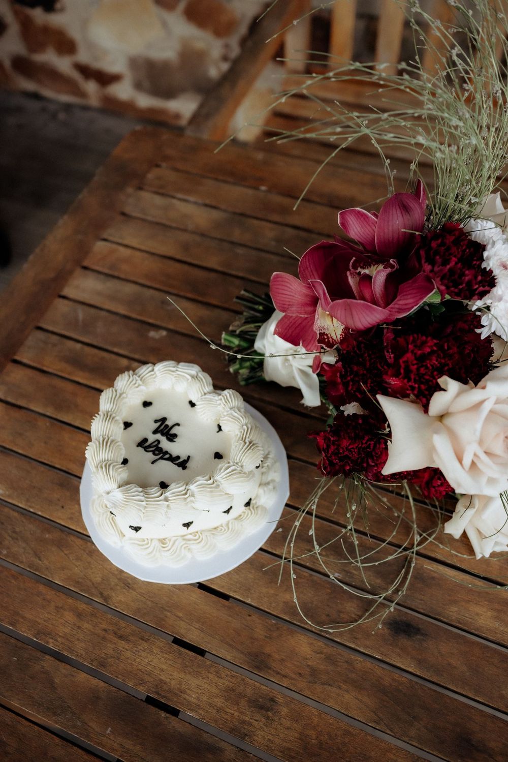 A white heart-shaped wedding cake beside Kaitlyn’s cream and burgundy flowers