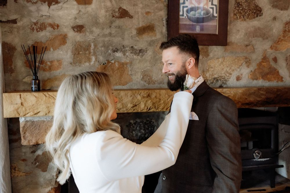 Kaitlyn straightening Russell’s tie beside the stone cottage fireplace at Piermont Retreat