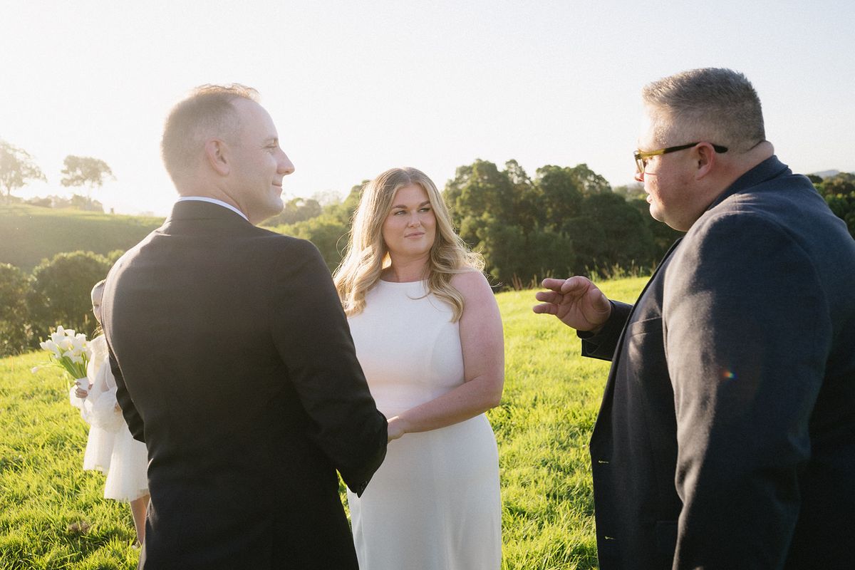 Libby and Daniel holding hands on the grass as Josh Withers leads their Byron Bay elopement ceremony