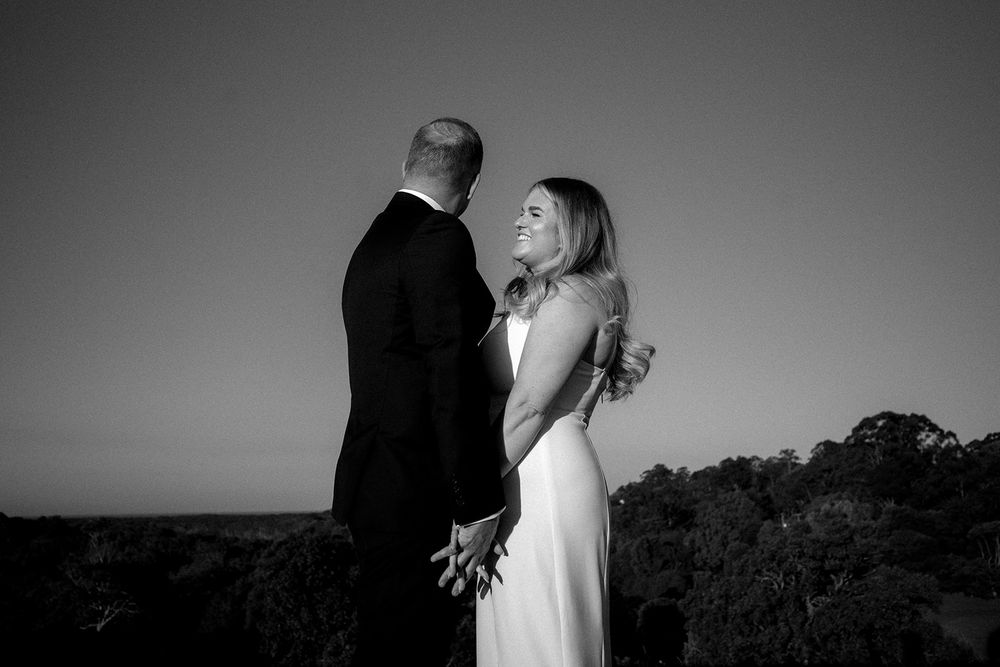Black and white photograph of Libby smiling at Daniel as they stand together holding hands