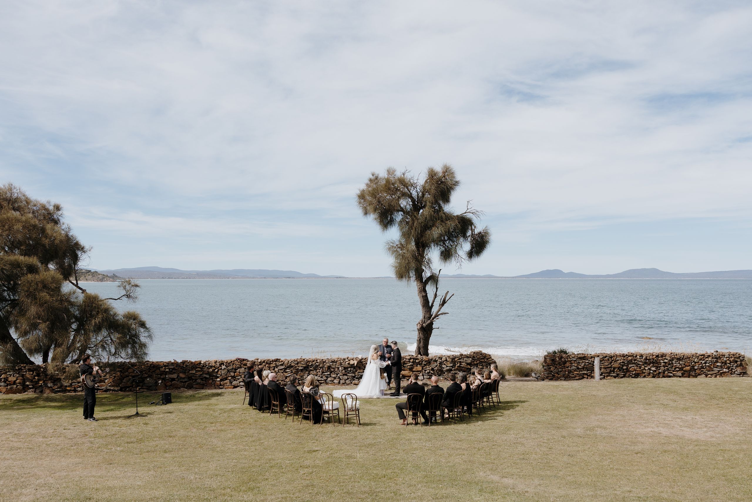 Wedding ceremony beside the water with guests seated on the lawn