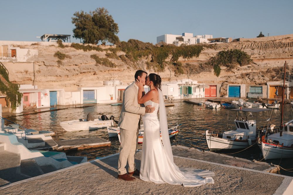 Tiegan and Michael kissing beside the colourful fishermen’s boathouses in Mandrakia, Milos
