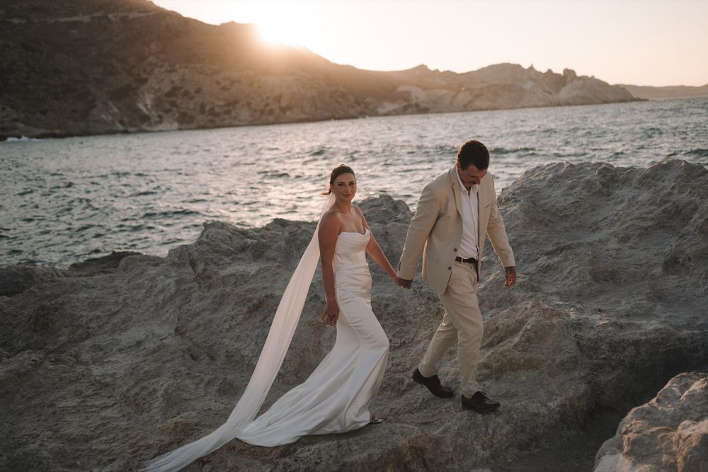 Tiegan and Michael walking hand in hand across the rocky coast at Sarakiniko, Milos